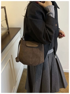 Sac seau en daim marron avec pompon décoratif porté par un mannequin de mode élégant