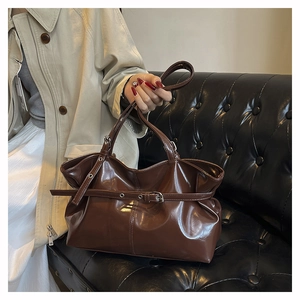 Close-up of glossy dark brown leather tote bag with stylish buckle strap on a vintage sofa