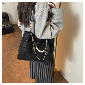 Detail of large black leopard embossed tote bag with decorative pearl and clover chain