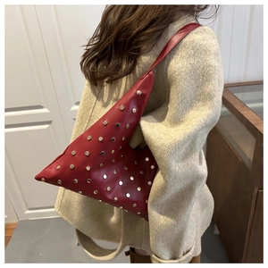 Detail of red leather tote bag with silver studs worn over a beige coat