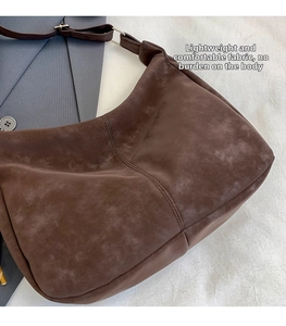 Detail of dark brown suede crossbody tote with vertical seam and metal buckle strap