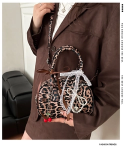 Detail of leopard print handbag with lace bow and cherry charm worn with brown suit