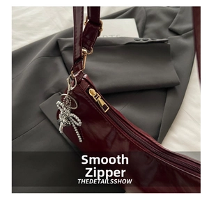 Detail of smooth gold zipper and dragonfly crystal charm on burgundy patent leather bag