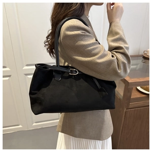 Detail view of black faux suede tote bag featuring sleek golden metal buckle and slim handles