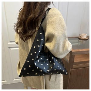 Detail of black leather tote bag featuring gold punk-style metal rivets and asymmetric design