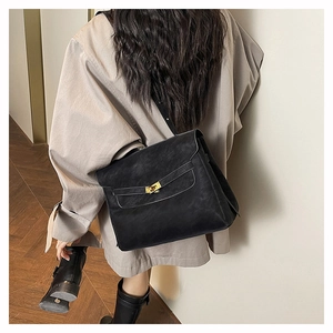 Detail of a large black leather tote with a gold twist lock clasp in a commute scene