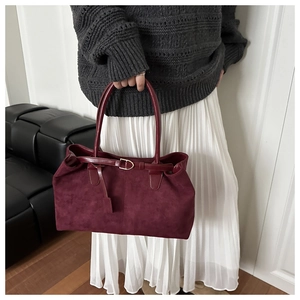 Macro detail of wine red suede tote bag featuring smooth leather handles and gold metal buckle