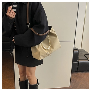 Detail of beige tote bag showing pearl chain handle and elegant brown shoulder strap