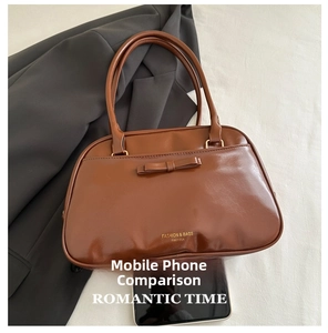 Borsa a mano marrone in ecopelle con fiocco accanto a un telefono per confronto taglia