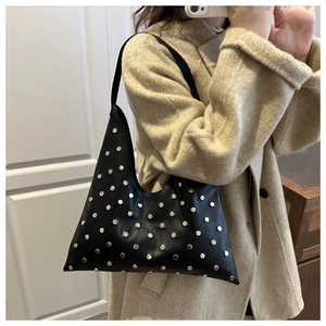 Side view of black leather hobo bag with metal rivets on a female model shoulder