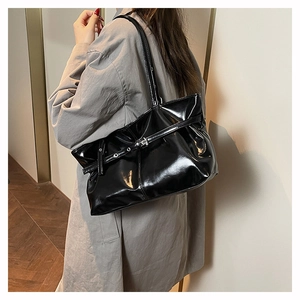 Detail of a black patent leather tote bag with metallic buckle strap and glossy finish