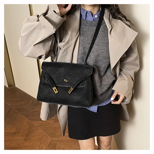 Detail of black trapezoid tote bag featuring a gold twist lock and textured matte finish