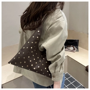 Detail of dark brown leather tote bag with gold rivets worn as an underarm bag