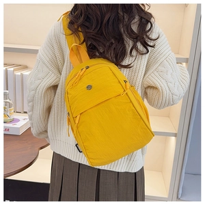 Detail showing bright yellow nylon backpack worn over white sweater in a lifestyle setting