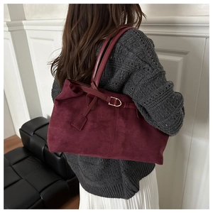 Detail of burgundy faux suede tote bag featuring slim straps and buckle accent on model