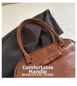 Dettaglio borsa a cuscino in pelle marrone con fiocco su sfondo di un blazer grigio