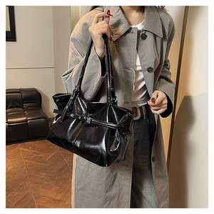 Detail of glossy black patent leather tote bag showing slim shoulder strap and buckle