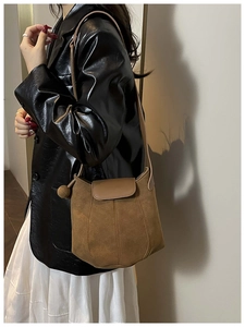 Détail d'un sac seau en daim marron avec pendentif boule décoratif et bandoulière fine