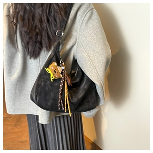 Close-up of black matte hobo bag with teddy bear charm and woven rope detail