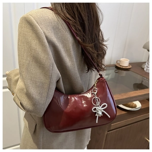 Detail of red crescent shoulder bag with glossy finish and silver bow pendant charm