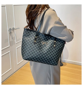 Detail of grey monogram tote bag with gold bow ornament and leather shoulder strap