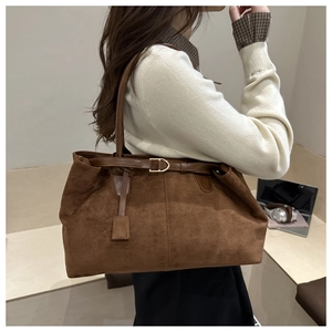 Detail of suede tote bag with decorative strap, gold buckle, and vertical stitching