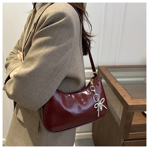 Detail of burgundy glossy patent leather underarm bag with silver bow charm on model