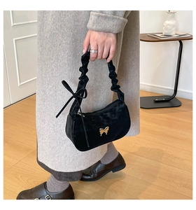 Detail of black velvet pleated handbag featuring gold butterfly buckle and ribbon bow