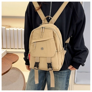 Close-up of beige nylon backpack featuring side red label and dual buckle strap details