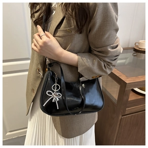 Detail of glossy black crescent shoulder bag with a sparkling silver bow charm