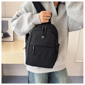 Detail of waterproof black nylon mini backpack with circular metal logo and zippers
