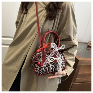 Close-up of leopard print handbag with red straps, cherry charm, and lace details