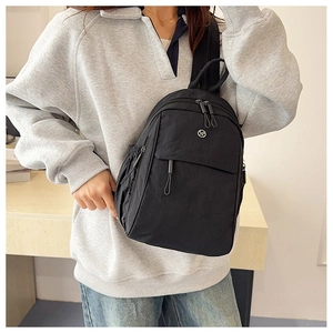 Detail of a black multi-pocket crossbody nylon bag worn by a model in a bright setting