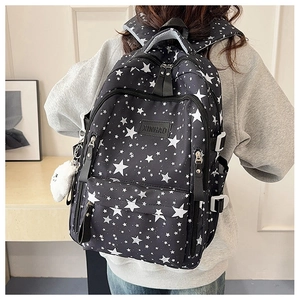 Macro detail of black nylon backpack featuring white star prints and plush charm pendant