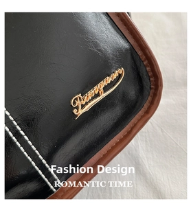Macro detail of textured black leather bag with brown trim and golden metal logo accent