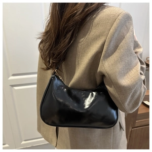 Side view of a glossy black patent leather underarm bag worn by a model in casual attire