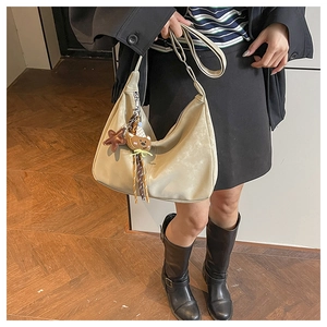 Detail of beige hobo bag with teddy bear charm and brown metal buckle hardware