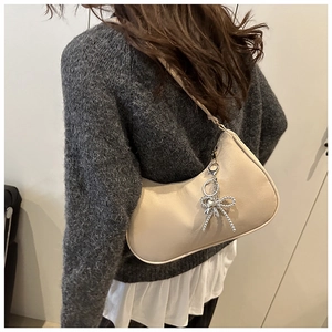 Dettaglio di una borsa hobo in pelle beige con pendente a cuore argento su maglia grigia