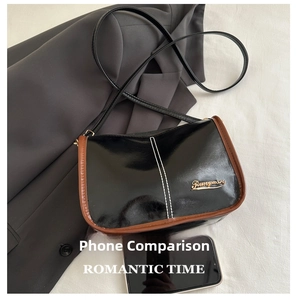 Detail of glossy black patent leather handbag with brown piping and gold logo lettering