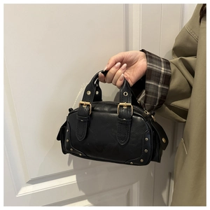 Detail of a black mini Boston bag with gold rivets and decorative buckles