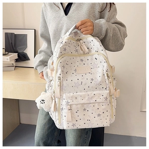 Detail of white star print backpack showing side pockets and plush bear keychain
