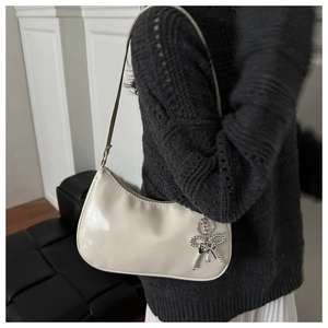 Close-up of cream patent leather handbag featuring a silver beaded butterfly charm detail