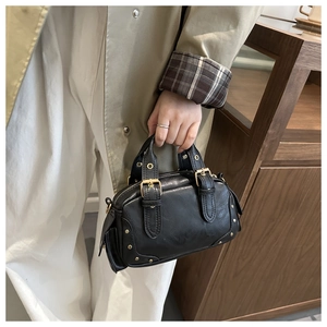 Retro black mini Boston bag with rivets held by model in a stylish trench coat
