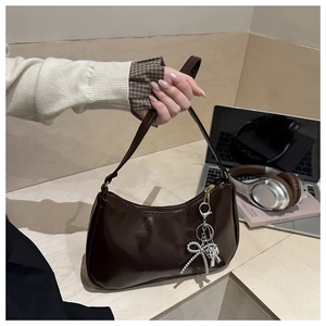 Dettaglio borsa in pelle verniciata marrone con ciondolo a fiocco argento e zip lucida