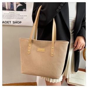 Close-up of beige corduroy tote bag featuring leather handles and gold rivet details