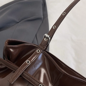 Dark brown patent leather tote bag with silver metal eyelets and adjustable strap