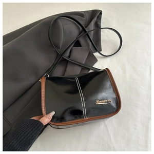 Detail of black patent leather shoulder bag with brown piping and gold logo lettering