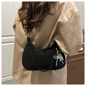 Detail of black crescent hobo bag with silver bow charm worn by a model in a warm interior