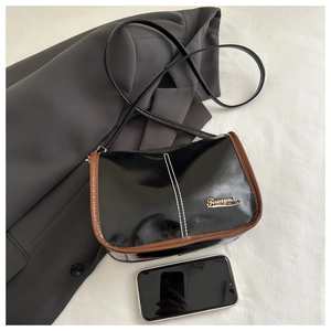 Close-up of stylish black and brown patent leather mini crossbody bag with gold logo