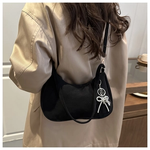 Dettaglio borsa hobo nera con ciondolo a fiocco argento indossata su un trench kaki